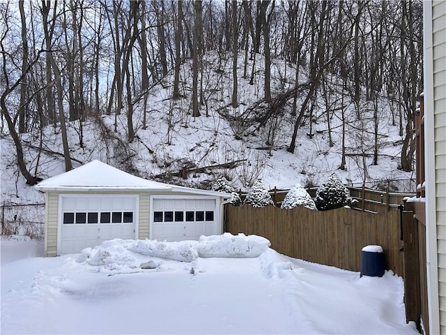 snow covered garage with a garage and fence