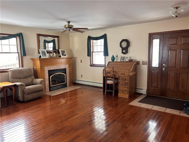 living room featuring ceiling fan, a tiled fireplace, wood-type flooring, and a baseboard radiator