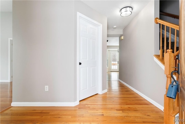 corridor with light wood-type flooring, stairway, and baseboards