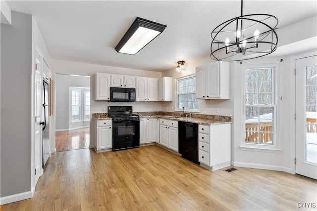 kitchen featuring pendant lighting, visible vents, white cabinets, a sink, and black appliances