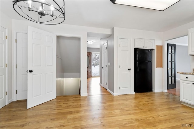 kitchen with freestanding refrigerator, light countertops, light wood-type flooring, white cabinetry, and a notable chandelier