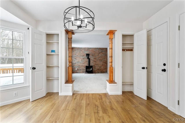 unfurnished dining area with a wood stove, light wood-style flooring, a wealth of natural light, and an inviting chandelier