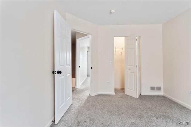 unfurnished bedroom featuring baseboards, a spacious closet, visible vents, and light colored carpet