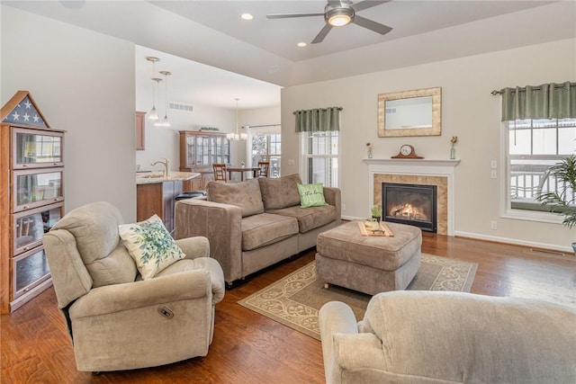 living room with ceiling fan with notable chandelier, dark wood-type flooring, and a tiled fireplace