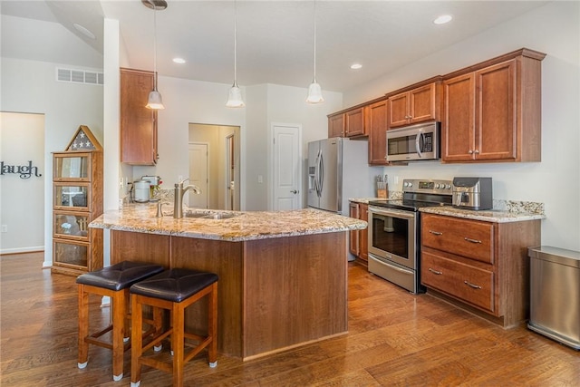 kitchen with stainless steel appliances, light stone counters, decorative light fixtures, sink, and kitchen peninsula