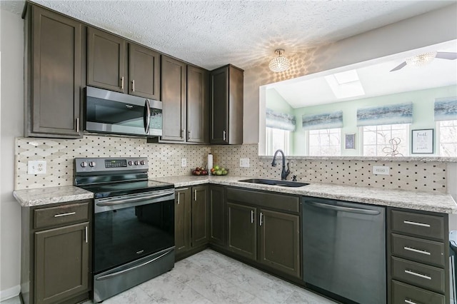 kitchen with appliances with stainless steel finishes, tasteful backsplash, dark brown cabinets, a skylight, and sink