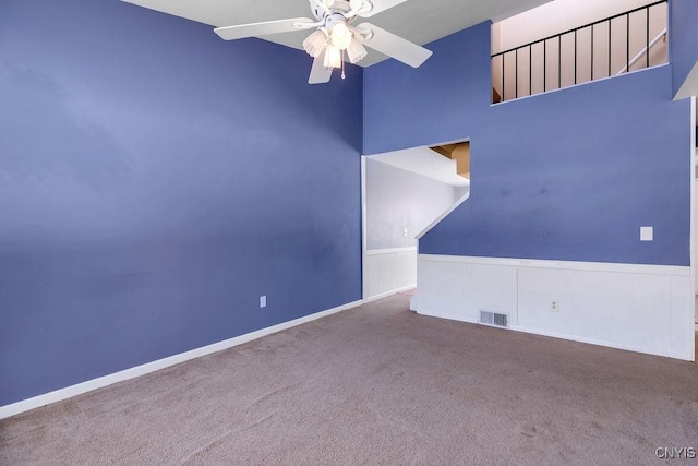 carpeted spare room featuring a towering ceiling and ceiling fan