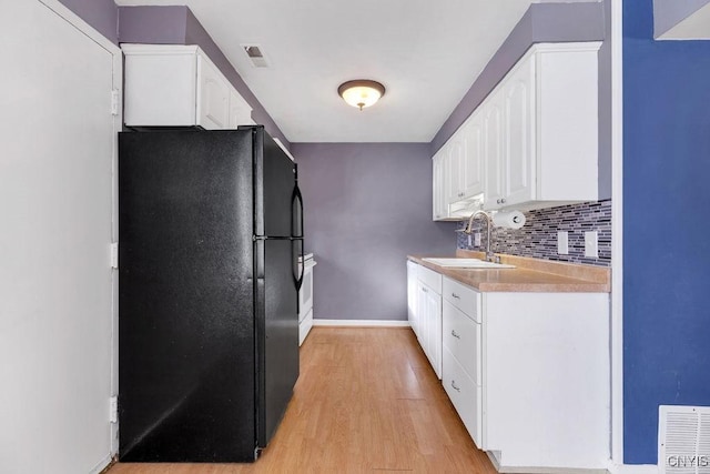 kitchen with sink, white cabinetry, light wood-type flooring, and black fridge