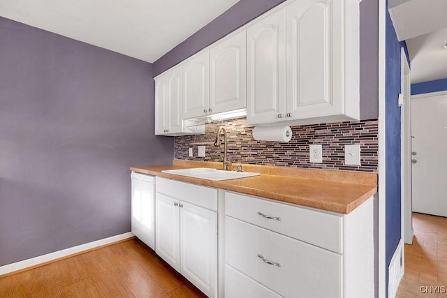 kitchen with tasteful backsplash, light wood-type flooring, sink, white dishwasher, and white cabinetry