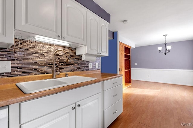 kitchen with light wood-type flooring, white cabinetry, sink, and decorative light fixtures