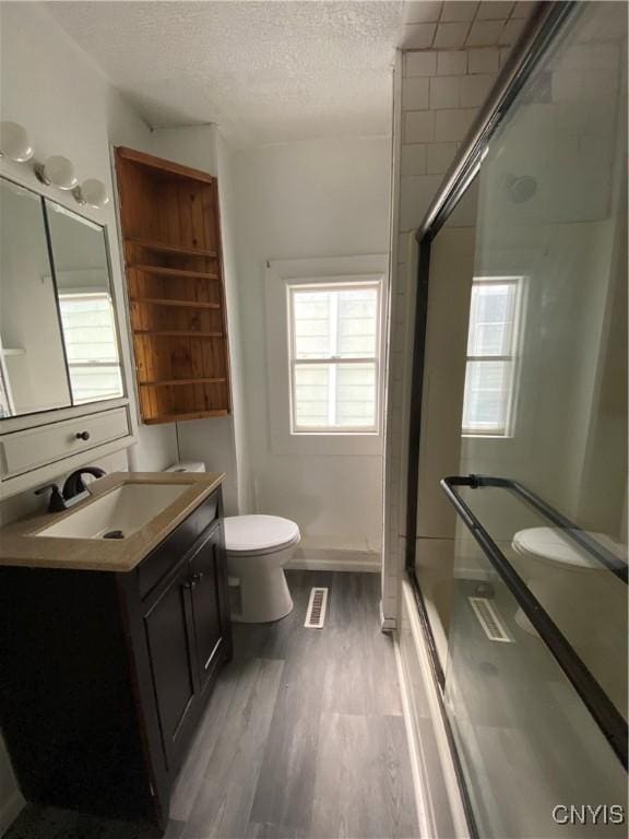 full bathroom with hardwood / wood-style flooring, toilet, combined bath / shower with glass door, a textured ceiling, and vanity