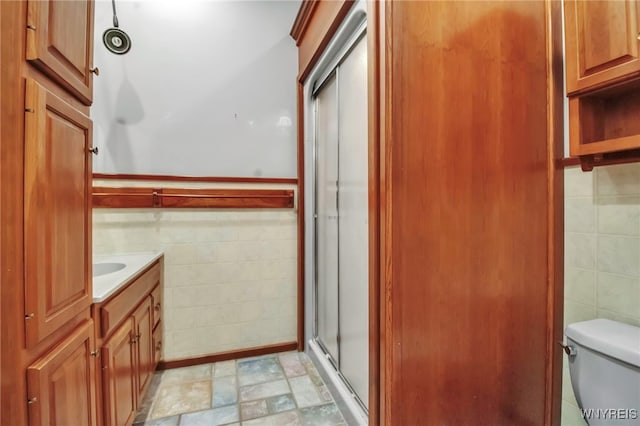 bathroom featuring toilet, tile walls, vanity, and an enclosed shower