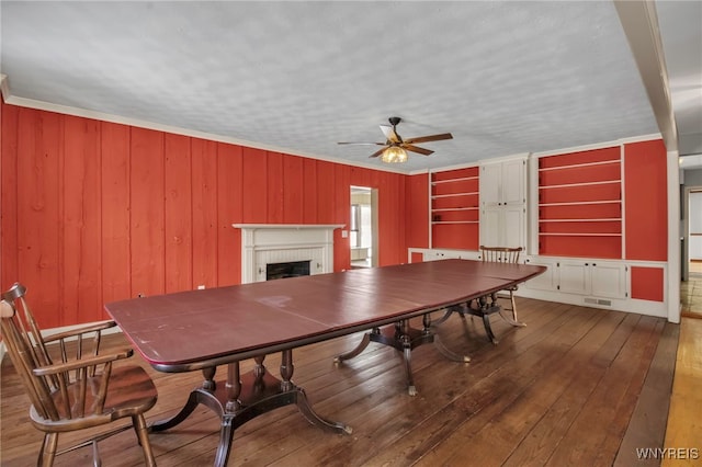 dining space with hardwood / wood-style floors, ceiling fan, a brick fireplace, and ornamental molding