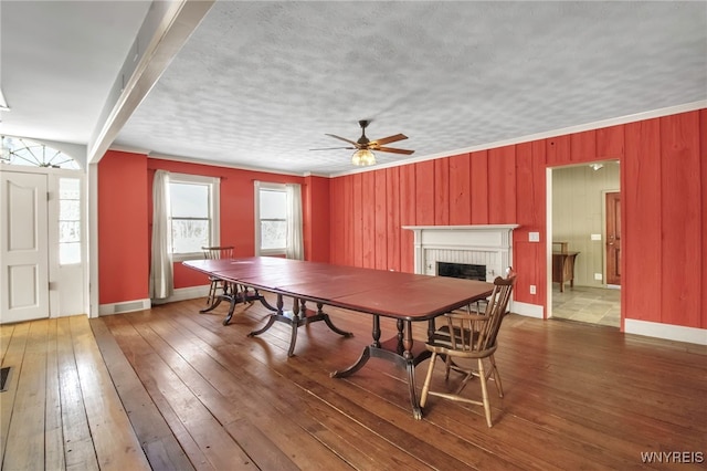 dining room with hardwood / wood-style flooring, a brick fireplace, ornamental molding, ceiling fan, and a textured ceiling