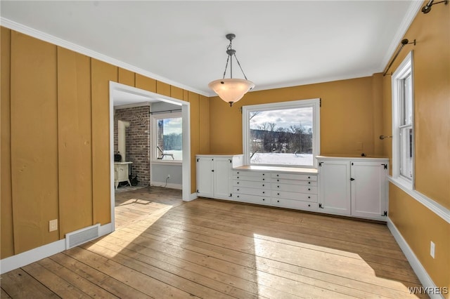 unfurnished dining area with a wood stove, light hardwood / wood-style floors, and ornamental molding