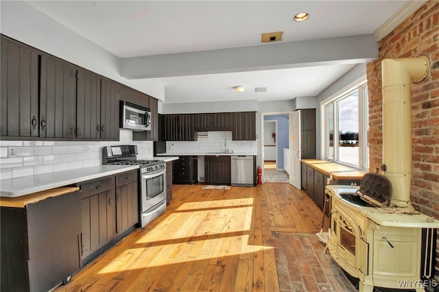 kitchen with appliances with stainless steel finishes, brick wall, dark brown cabinets, and backsplash