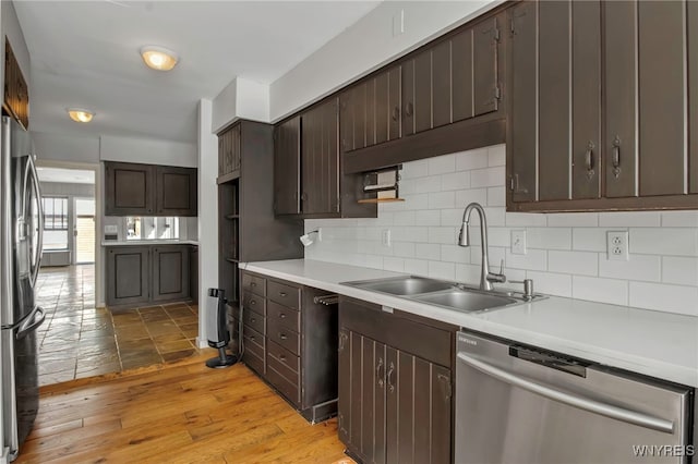 kitchen featuring light wood-type flooring, sink, dark brown cabinets, tasteful backsplash, and appliances with stainless steel finishes