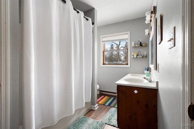 full bathroom featuring hardwood / wood-style flooring, a baseboard heating unit, toilet, shower / bath combo with shower curtain, and vanity