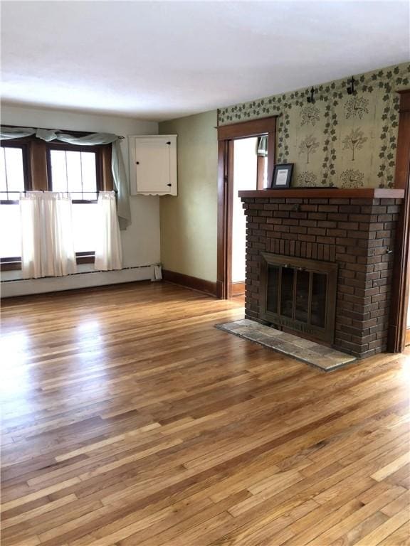 unfurnished living room featuring a baseboard heating unit, baseboards, light wood-style floors, wallpapered walls, and a brick fireplace