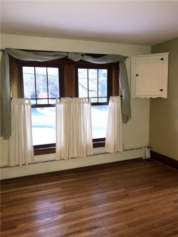 unfurnished room featuring dark wood-type flooring, plenty of natural light, and baseboards