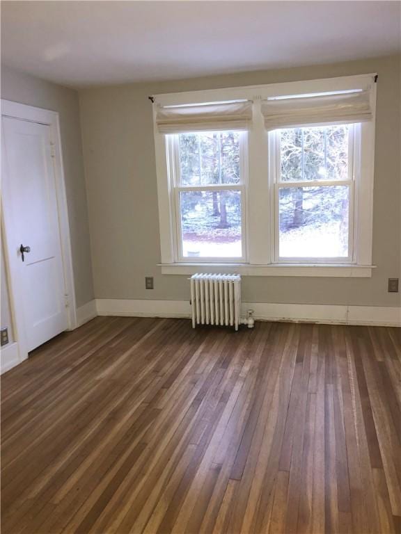 spare room with radiator heating unit, baseboards, and dark wood finished floors