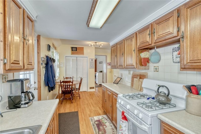 kitchen with light hardwood / wood-style floors, white gas range, and backsplash