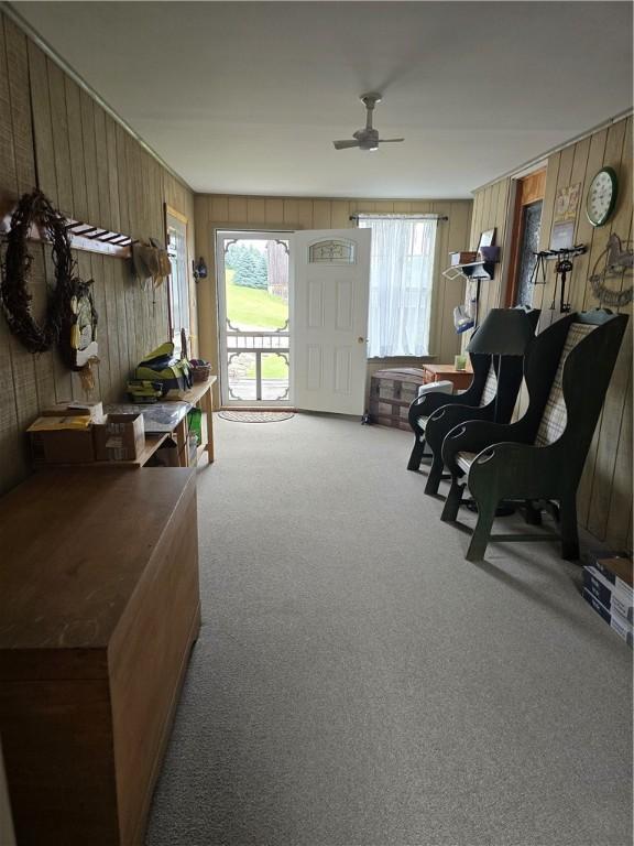 carpeted living room with ceiling fan and wood walls