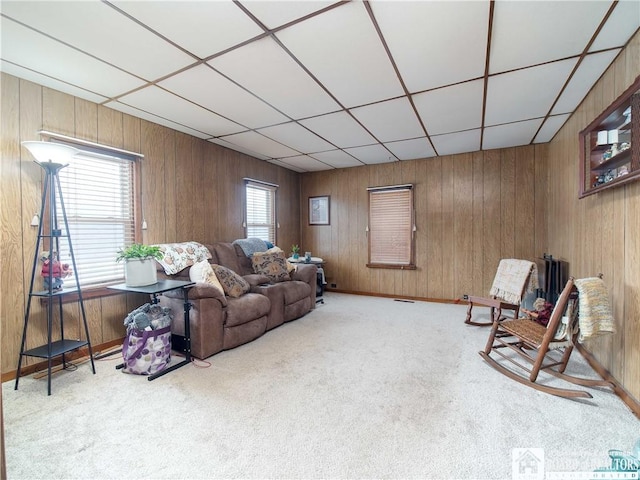 living room with a drop ceiling, light carpet, and wooden walls