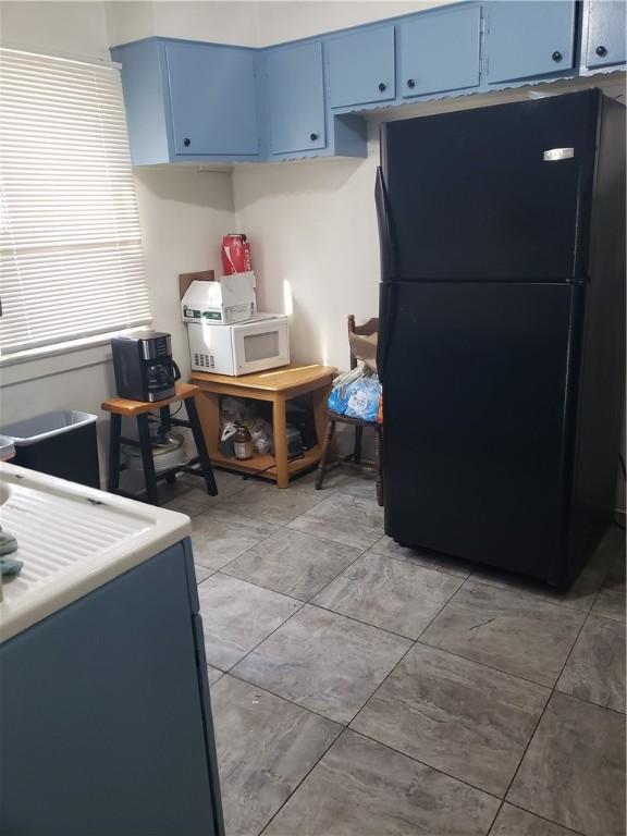 kitchen with light countertops, white microwave, freestanding refrigerator, and blue cabinets