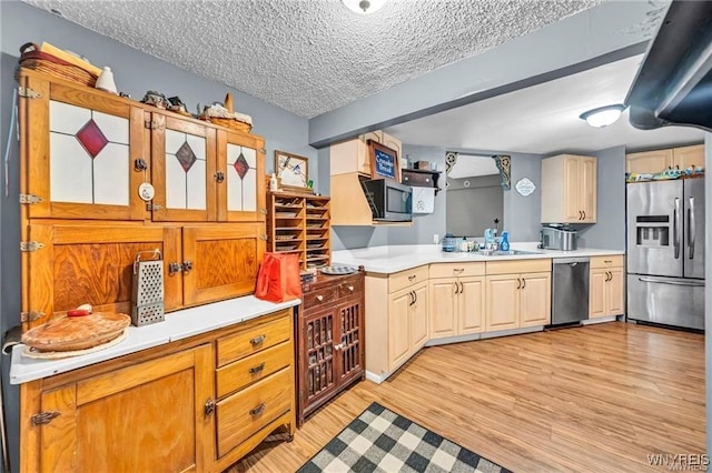 kitchen with a textured ceiling, appliances with stainless steel finishes, sink, and light hardwood / wood-style floors