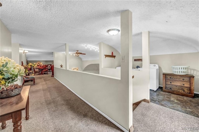 hallway with a textured ceiling, washer / dryer, and dark colored carpet