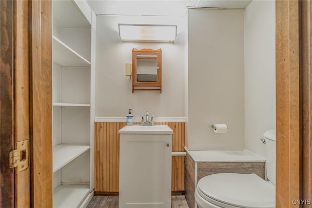 bathroom with toilet, wood-type flooring, wood walls, and vanity