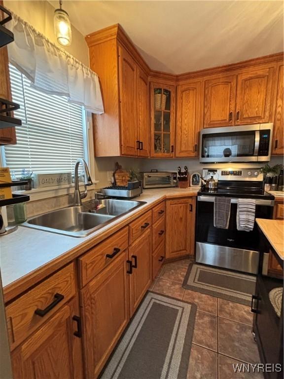 kitchen with appliances with stainless steel finishes, sink, dark tile patterned floors, and decorative light fixtures