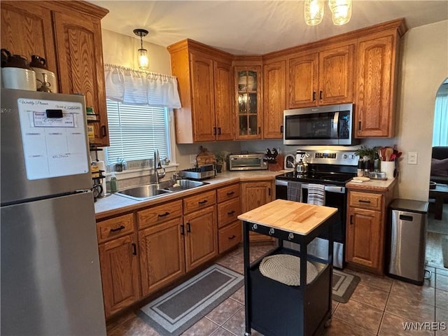 kitchen with sink, dark tile patterned floors, appliances with stainless steel finishes, and decorative light fixtures