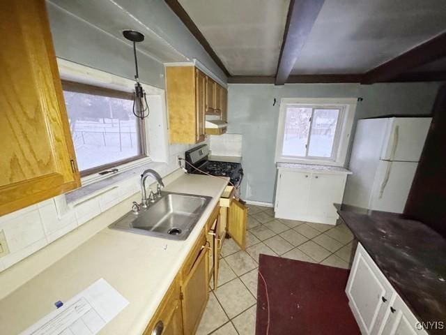 kitchen with hanging light fixtures, white refrigerator, sink, backsplash, and light tile patterned floors