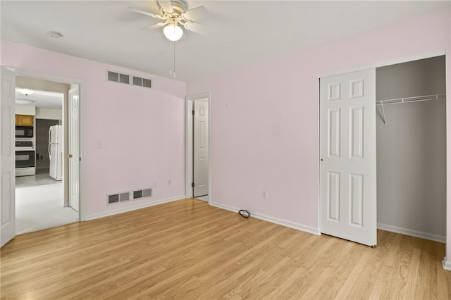 unfurnished bedroom with ceiling fan, white fridge, a closet, and light hardwood / wood-style flooring