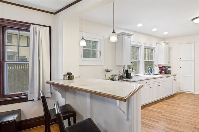 kitchen featuring white cabinetry, kitchen peninsula, decorative light fixtures, and a kitchen bar