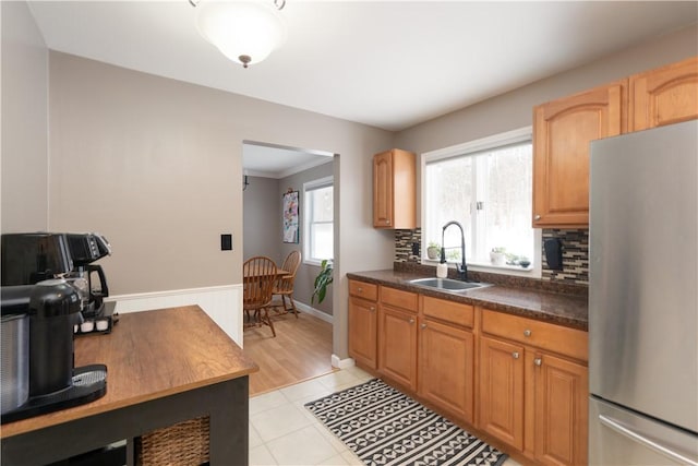 kitchen with stainless steel refrigerator, backsplash, light tile patterned floors, ornamental molding, and sink