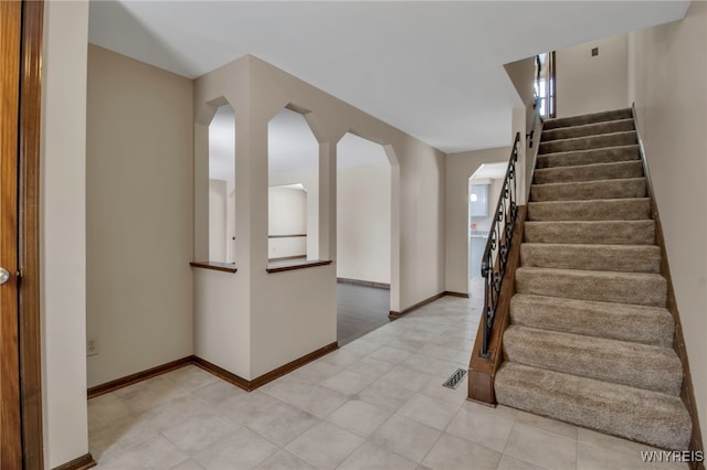 entryway featuring stairway, light tile patterned floors, baseboards, visible vents, and arched walkways