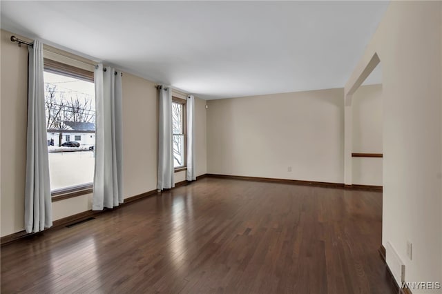 spare room featuring visible vents, plenty of natural light, baseboards, and dark wood-type flooring