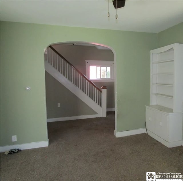 interior space featuring arched walkways, dark carpet, and baseboards