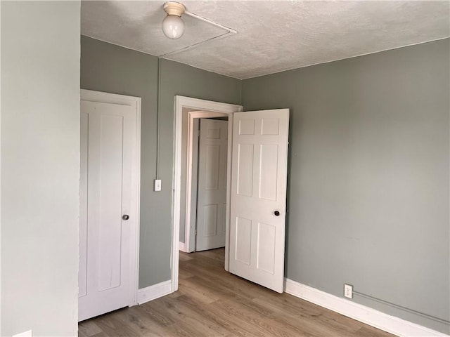 unfurnished bedroom featuring a textured ceiling, light wood-style flooring, and baseboards