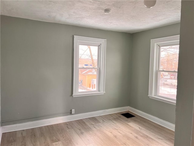 unfurnished room with visible vents, light wood finished floors, baseboards, and a textured ceiling