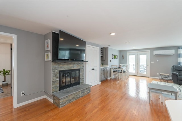 living room with baseboards, a stone fireplace, a wall unit AC, and light wood-style floors