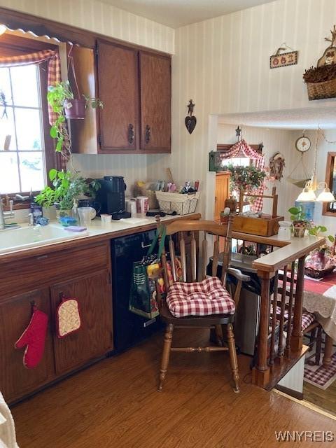 kitchen with wallpapered walls, dishwasher, wood finished floors, light countertops, and a sink