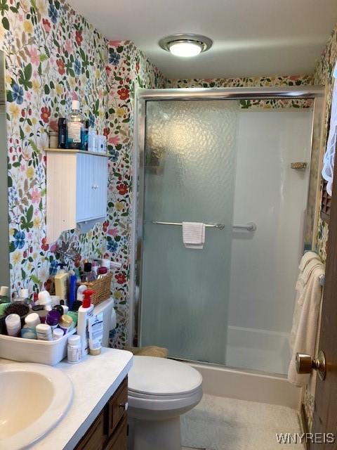 full bath featuring toilet, a stall shower, vanity, and wallpapered walls