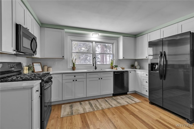 kitchen with white cabinets, black appliances, light countertops, and a sink