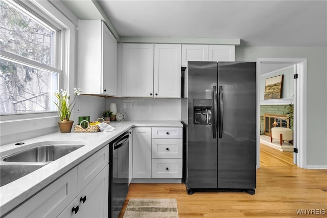 kitchen featuring refrigerator with ice dispenser, dishwasher, a stone fireplace, light wood-type flooring, and white cabinetry