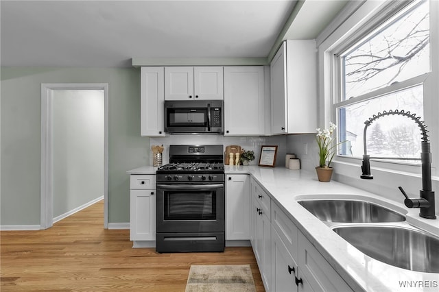 kitchen with a sink, white cabinetry, baseboards, light wood-type flooring, and gas stove