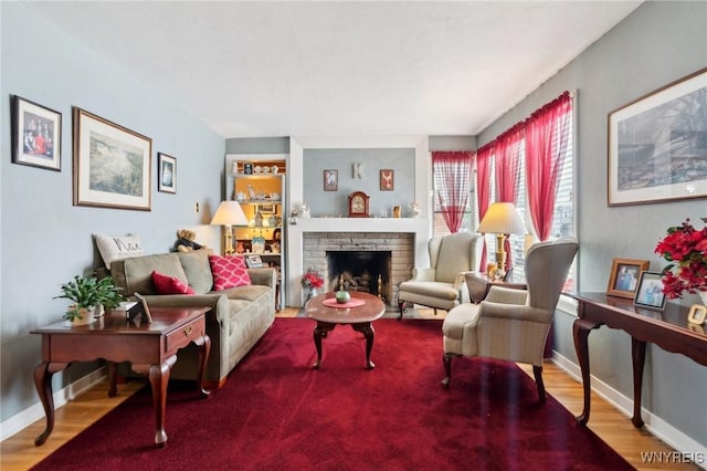 living room with a brick fireplace, baseboards, and wood finished floors